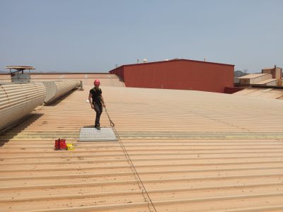 Trabajador de taludia en una cubierta industrial instalando pasillos técnicos para lucernarios.