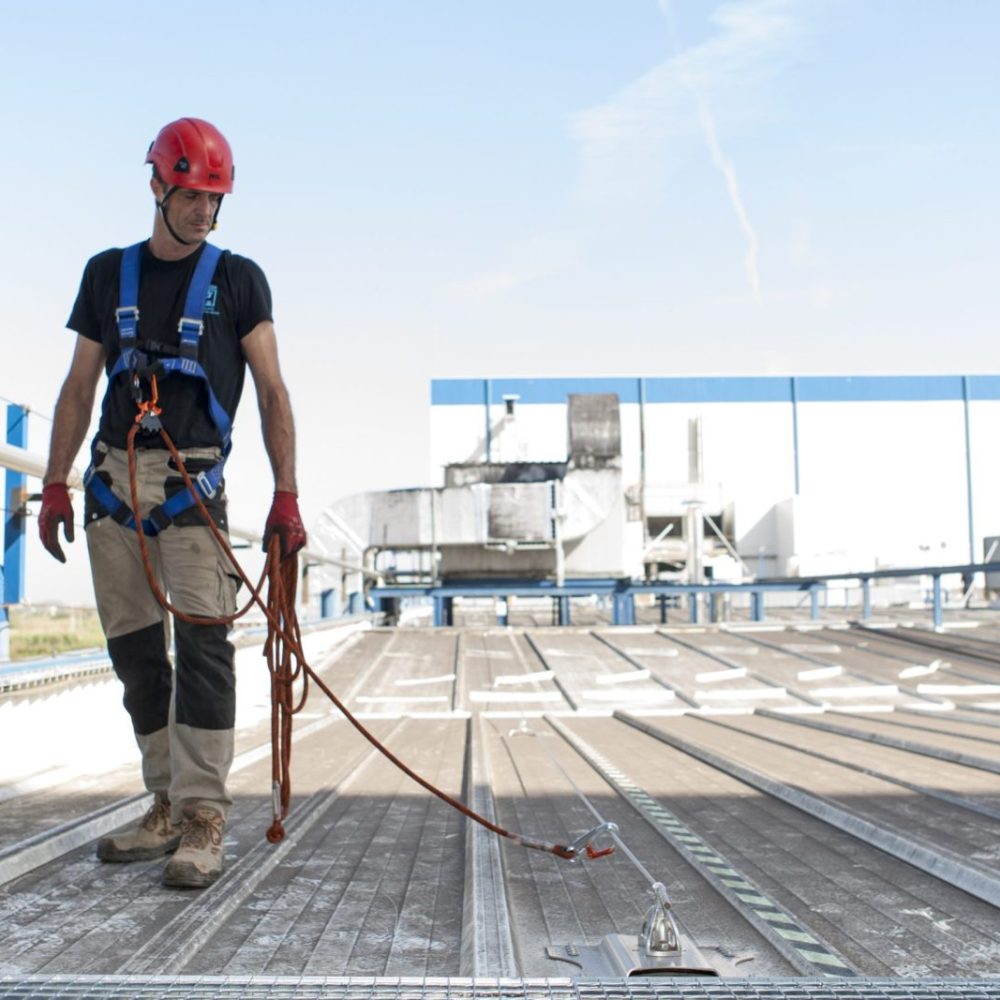 Trabajador en altura enganchado a línea de vida, sobre la cubierta de una industria.